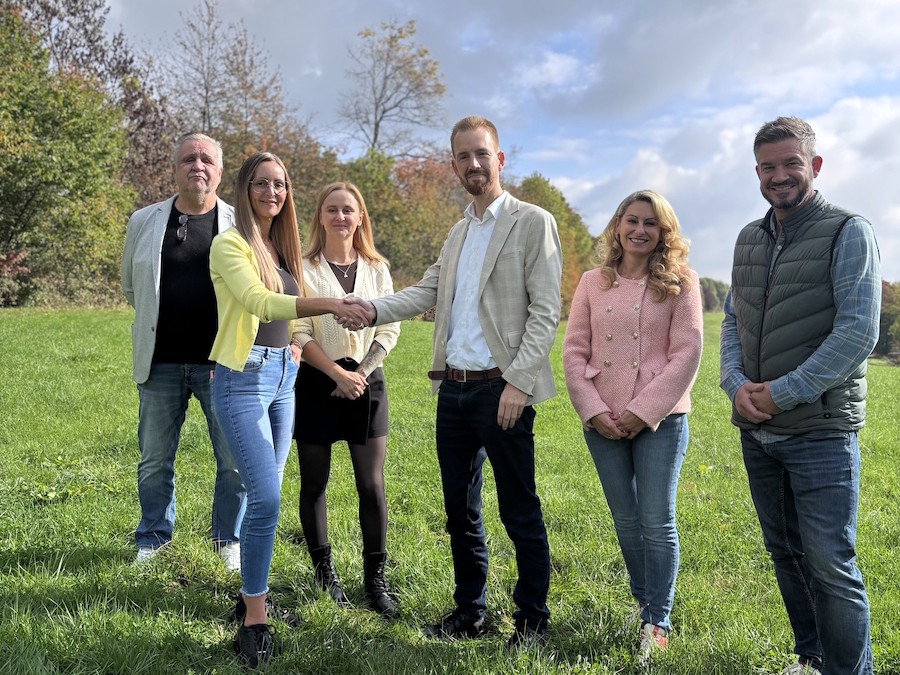 Sechs Personen stehen im Freien, während zwei von ihnen sich die Hände schütteln.